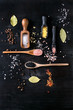 Variety of different colorful salt yellow saffron, pink, black himalayan, white sea and fleur de sel in wooden spoons with black, chili, allspice pepper over black burnt wood background. Top view