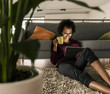 © Westend61 - Smiling young woman at home holding cup and tablet