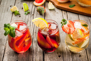 Traditional summer drink sangria - red, pink and white. With champagne, pink and red wine, strawberries, oranges, lemon, green apple and grapefruit. On a wooden rustic table, copy space 