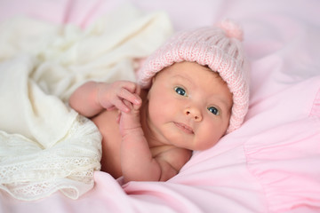 newborn baby girl in pink knitted hat on pink blanket