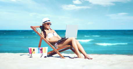 Wall Mural - Young, beautiful and sexy woman with the notebook relaxing on the beach.