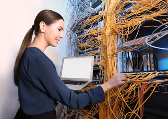 Beautiful young engineer with laptop in server room