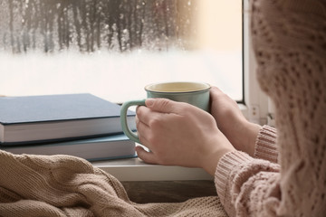 Young woman with cup of hot tea near window, closeup