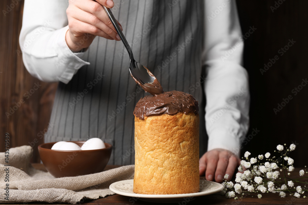 Woman decorating Easter cake with chocolate coating on table