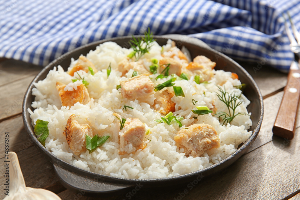 Delicious rice with chicken in pan on wooden table
