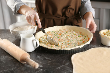 Woman making delicious chicken pot pie on kitchen table