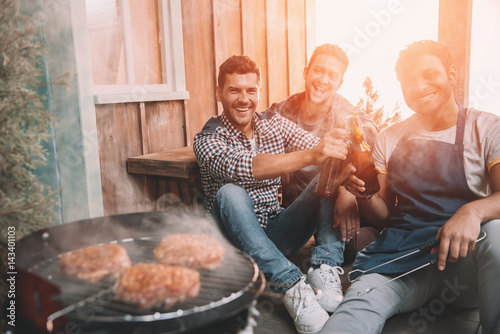 Fotomural happy young friends making barbecue and drinking beer on porch with back light