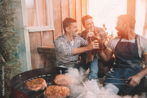 Fotografie, Obraz happy young friends making barbecue and drinking beer on porch with back light