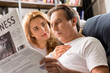 © LIGHTFIELD STUDIOS - Happy middle aged couple sitting on bed, man reading newspaper at home