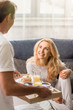 © LIGHTFIELD STUDIOS - Man bringing tray with tasty breakfast to happy blonde woman on bed