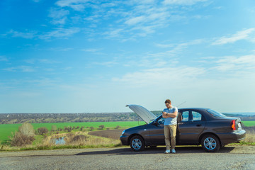 Wall Mural - Angry young man waiting a help while sitting near the broken car