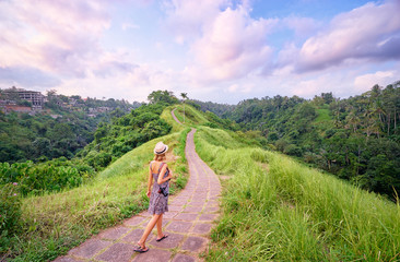 Wall Mural - Tourism and travel. Young woman in hat with camera walking on path, enjoying beautiful view.