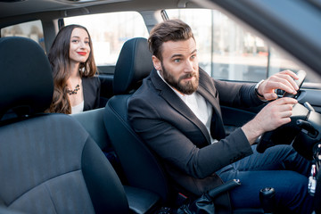 Wall Mural - Businesswoman on the backseat with elegant man driving a car in the city. Worried about a delay to an important meeting