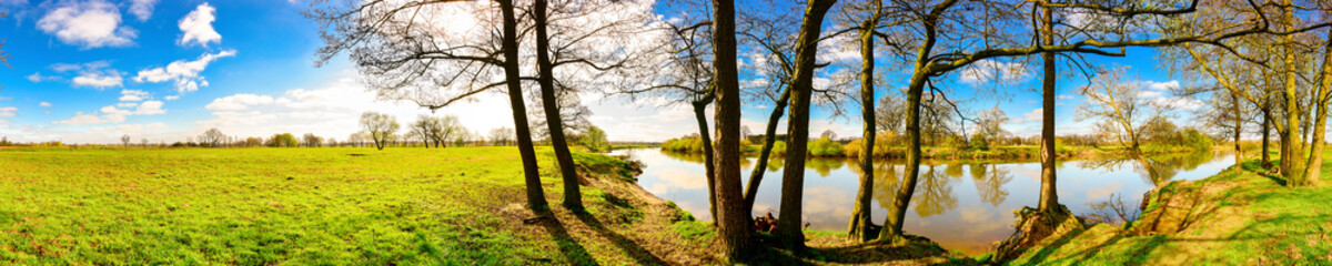 Wall Mural - Panorama einer Landschaft im Frühling mit blauen Himmel, Sonne, Wiese und Fluss