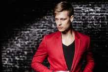 The Guy Is A Model In A Red Jacket. Beautiful Brown-haired Man On A Black Background.