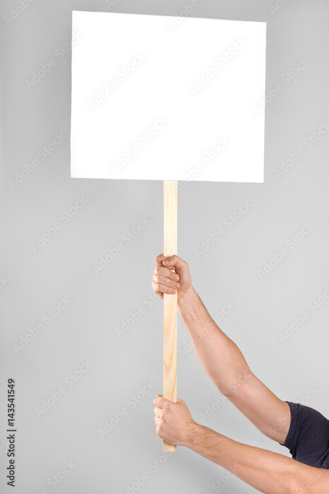 Male hands holding blank banner on wooden stick against light background