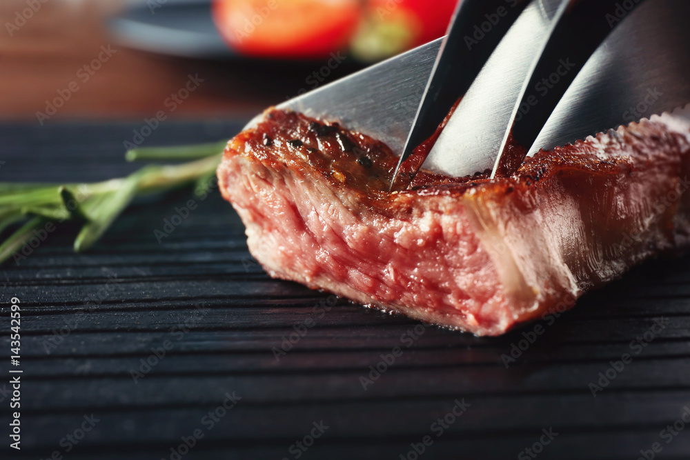 Cutting delicious medium rare steak on black wooden board