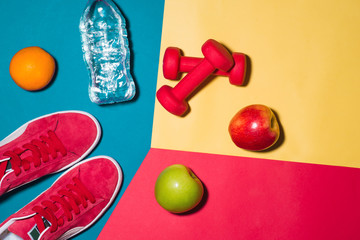 Wall Mural - Sport concept. Fitness equipment. Sneakers, water, apple, dumbbell on colorful background.