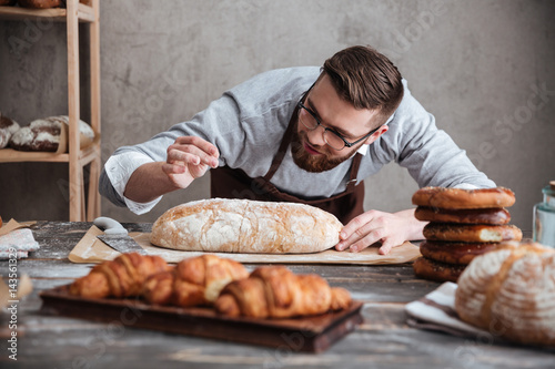 Fotografía Concentrated man baker standing at bakery near bread.