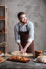 Sticker - Happy young man baker standing at bakery cut the bread.