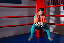 Young Female Boxer With A Towel Around Her Neck Sitting In Regular Boxing Ring