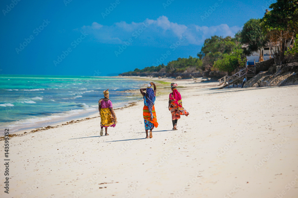 Three women walking on the beach in Jambiani, Zanzibar island, Tanzania - obrazy, fototapety, plakaty 