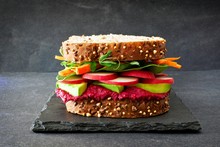 Superfood Sandwich With Beet Hummus, Avocado, Vegetables And Greens, On Whole Grain Bread Against A Slate Background