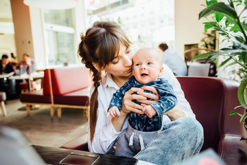 Beautiful young mother working with laptop computer and breastfeeding, holding and nursing her newborn baby at cafe. Mom - business woman feeding newborn.