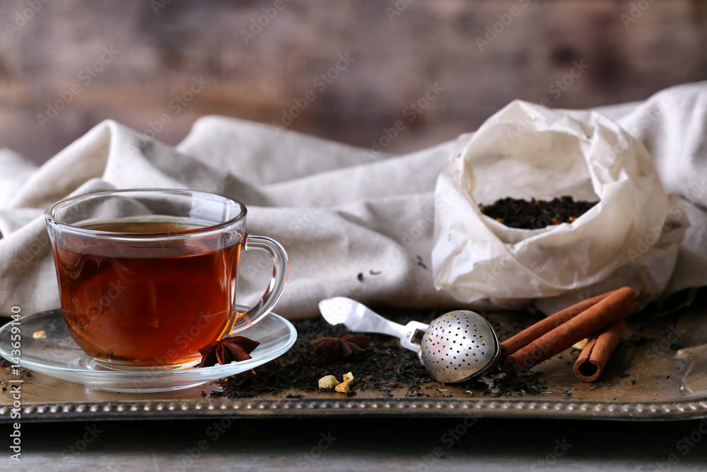 Cup of tea with spices and strainer on tray