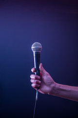hand with microphone on a black background, the music concept, beautiful lighting on the stage