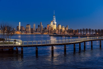 Fototapete - New York City Financial District skyscrapers at sunset and Hudson River from Hoboken promenade. Lower Manhattan skyline and pedestrian bridge from New Jersey