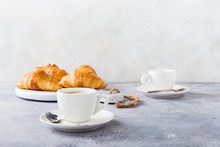 White Cups Of Coffee And Croissants On Light Gray Background, Selective Focus. Healthy Breakfast Concept With Copy Space.