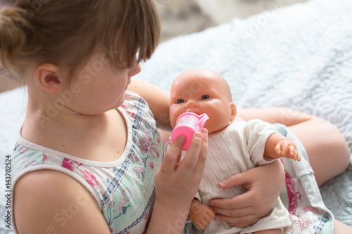 Kid girl playing with doll, feeding doll bottle Poster Mural XXL
