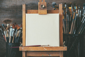 artistic equipment in a artist studio: empty artist canvas on wooden easel and paint brushes retro t