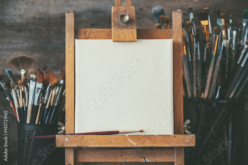 Fotografía Artistic equipment in a artist studio: empty artist canvas on wooden easel and paint brushes Retro toned photo