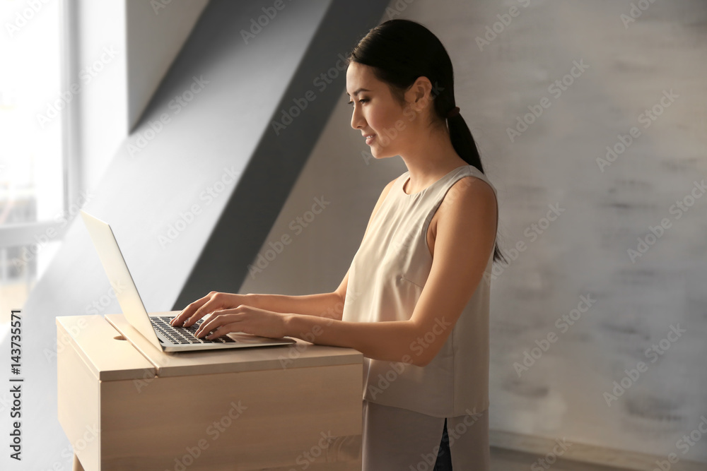 Asian woman typing on laptop at stand-up workplace