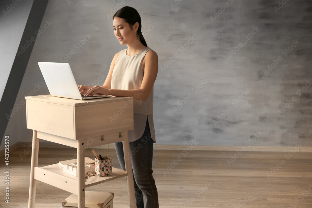 Asian woman typing on laptop at stand-up workplace