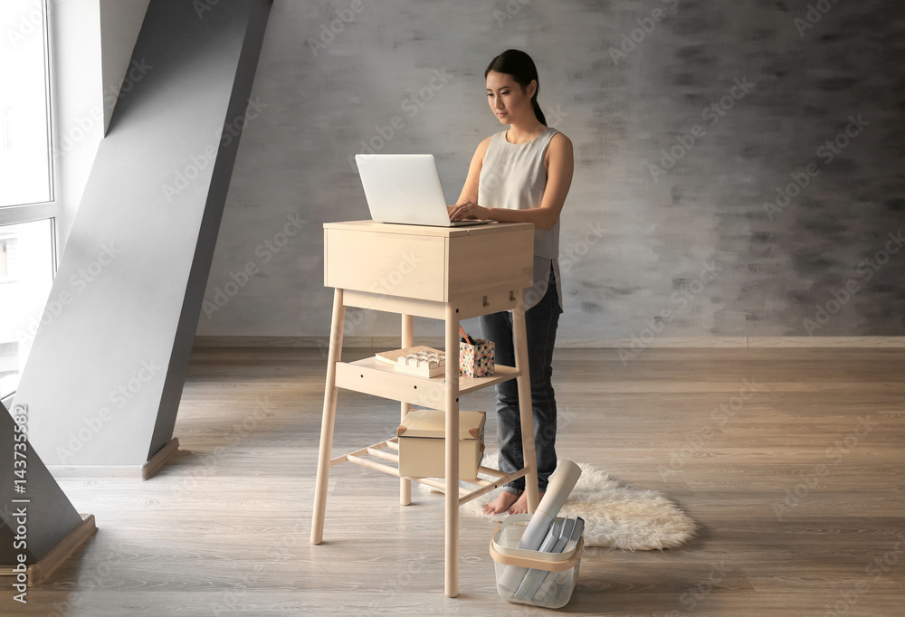 Asian woman typing on laptop at stand-up workplace