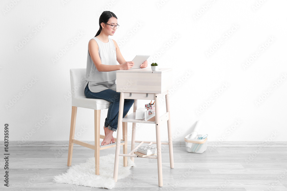 Asian woman with tablet computer sitting at high desk in room