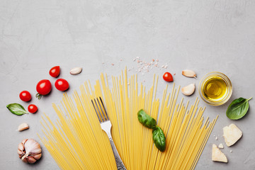 Wall Mural - Italian food background with uncooked spaghetti, tomato, basil leaves, cheese, garlic and olive oil on gray stone table top view in flat lay style. Ingredients for cooking pasta with space for recipe.