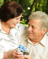 Mature happy smiling couple embracing in park with gift