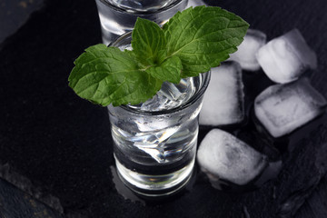 Vodka in shot glasses and ice on rustic wood background