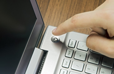 Closeup view of a hand with a finger, press the power button on metallic silver laptop keyboard, lying on a wooden mat blur