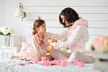 Young mother is fixing jewelry on her daughter's neck