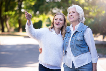 Positive aged woman and mature daughter walking in the park