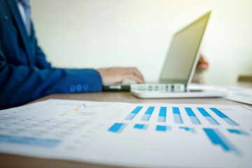 Wall Mural - Image of business, Business man working at office with laptop and graph data documents on his desk, blurred background.