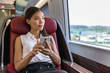 Asian woman relaxing in train seat while using smartphone app. Chinese businesswoman enjoying view texting on mobile phone. Travel lifestyle.