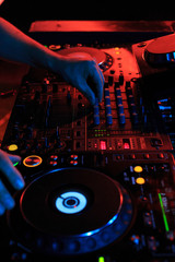 DJ playing music in night club party. Turntable equipment in dark red