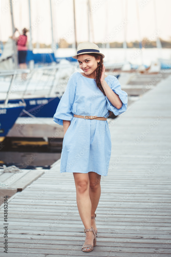 Portrait of white Caucasian brunette woman with tanned skin in blue dress  by seashore lakeshore with yachts boats on background on water, lifestyle  summer hobby leisure concept Stock Photo | Adobe Stock