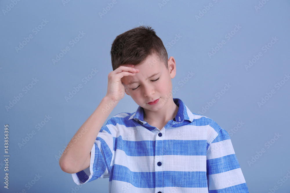 Cute boy suffering from headache on color background